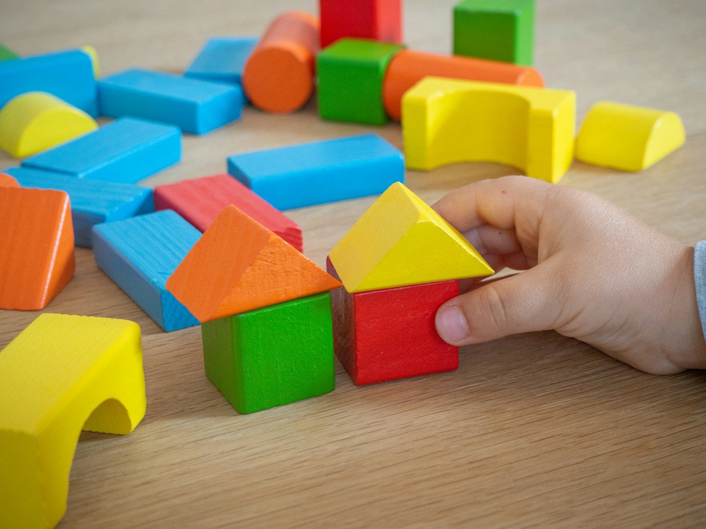 Hands arranging red, yellow, blue, and green wooden building blocks