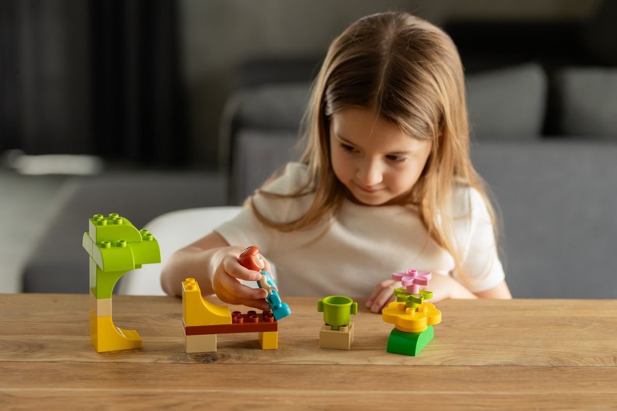 A child playing with a little figure and colorful toy scenery on a table